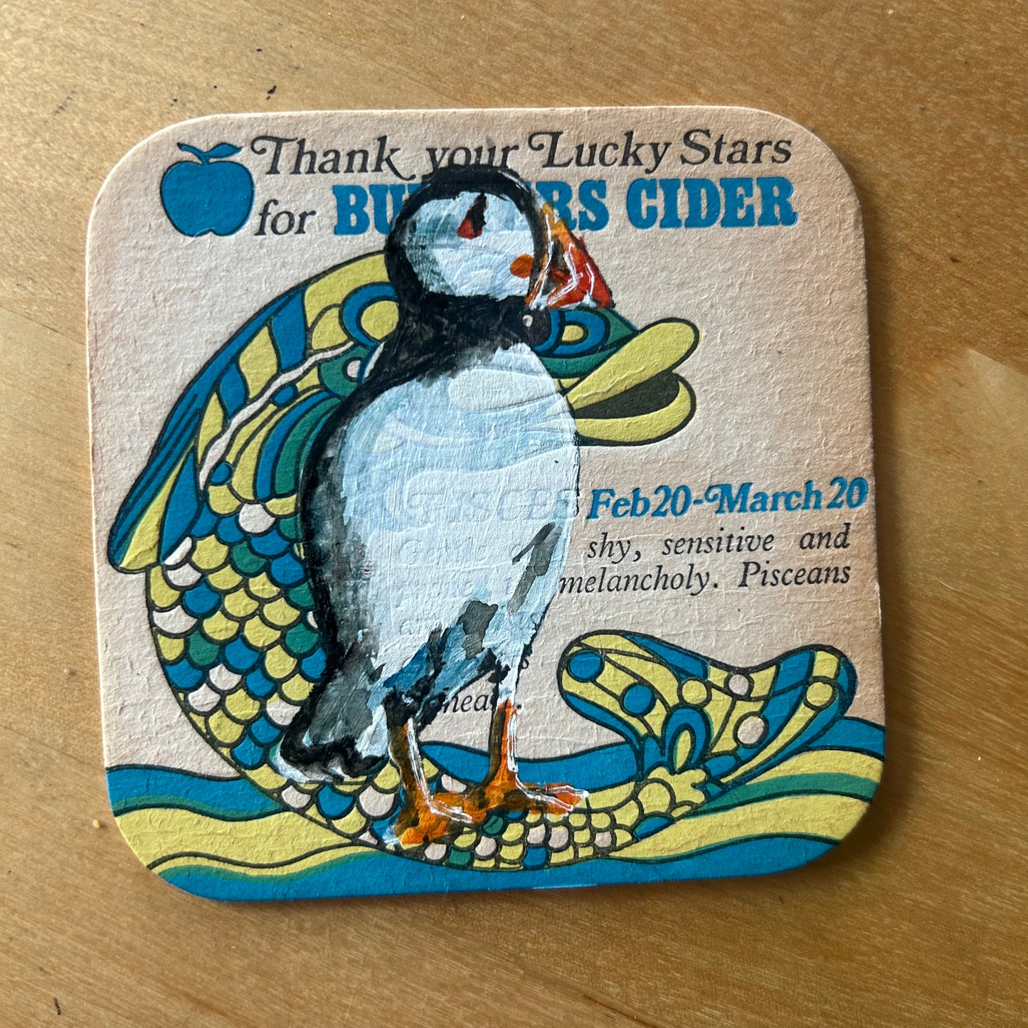 A Puffin painted onto a 1970s Bulmer’s Cider Zodiac drinks mat (Pisces). Beermat painting. Watercolour.