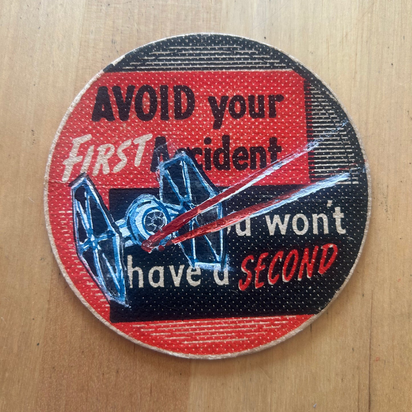 A Tie Fighter painted on a ‘Avoid Your First Accident’ Beermat from the 1950s. Beermat painting. Watercolour.