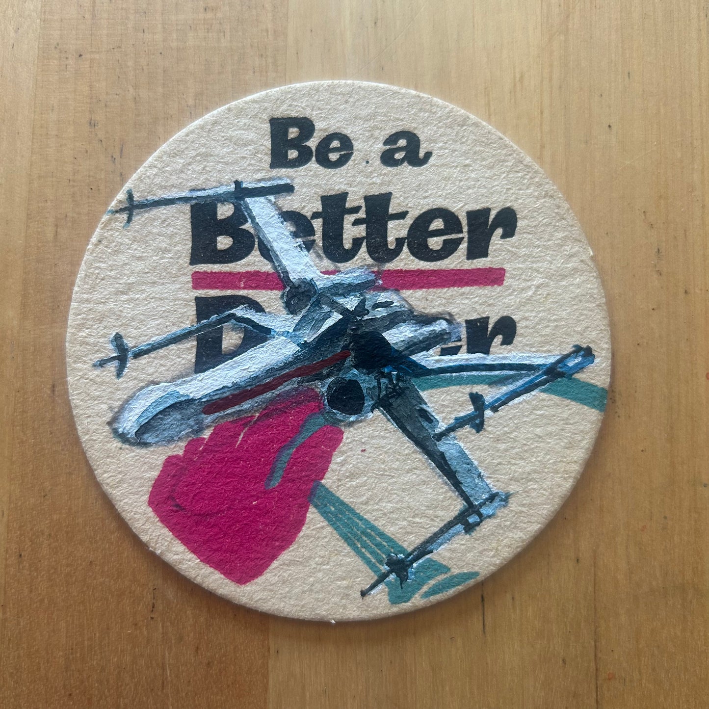 An X-Wing painted on a ‘Be a Better Driver’ Beermat from the 1950s. Beermat painting. Watercolour.